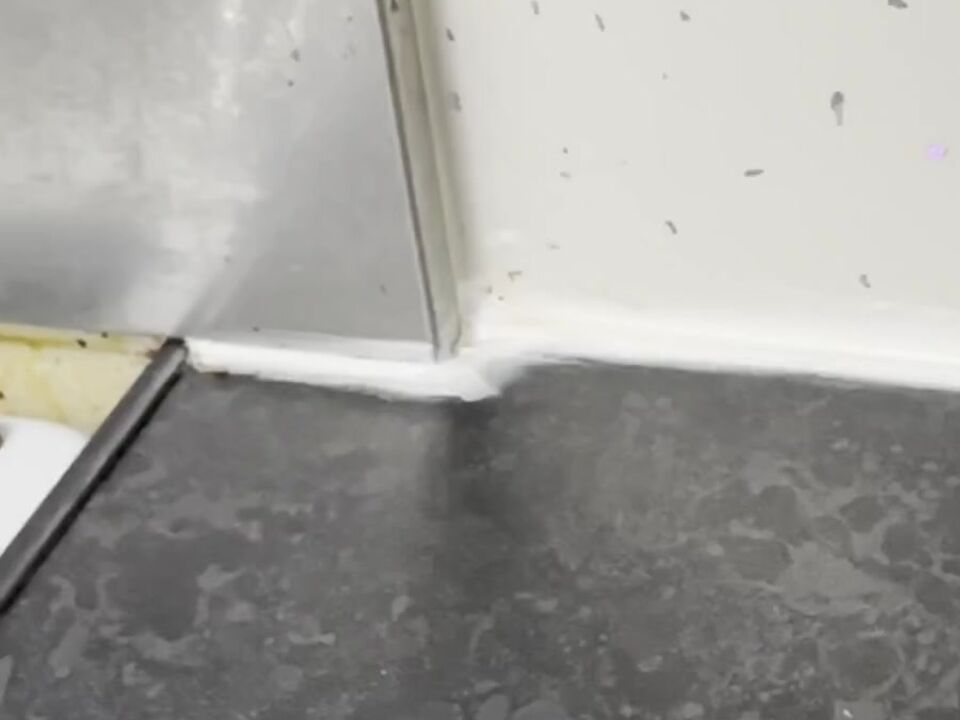 White sealant ending in a blob where the wall panel meets a metal trim next to the cooker