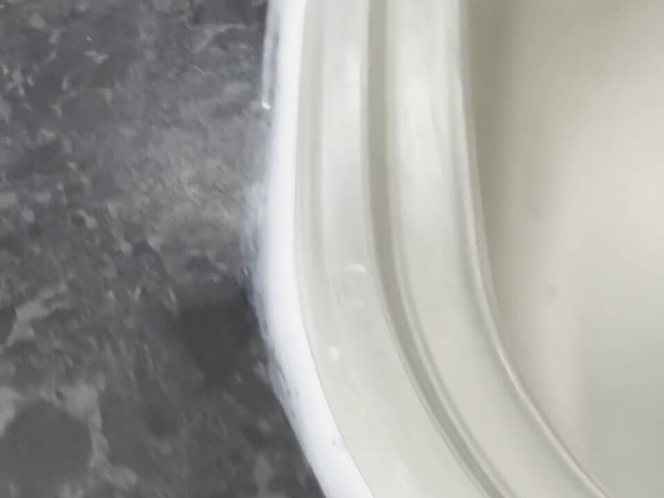 Uneven white sealant round the side of a steel sink, with a white haze smeared on the black worktop